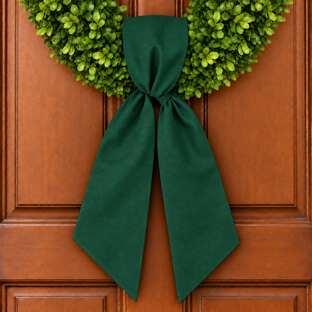 Boxwood wreath on wooden door with hunter green wreath sash tied to it.