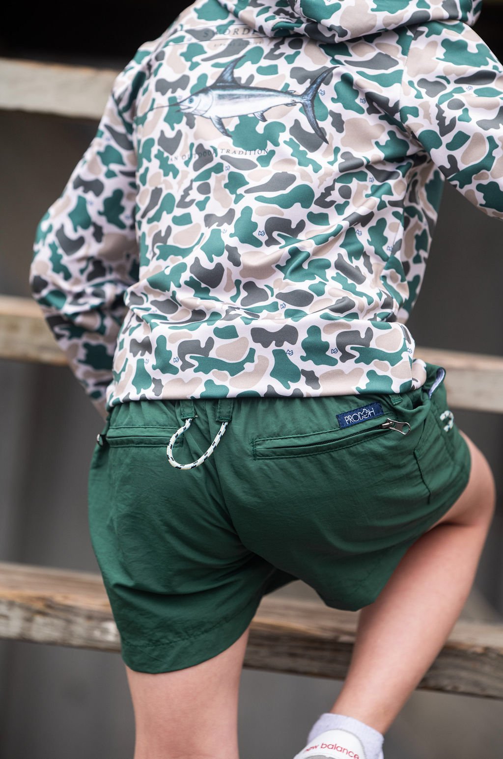 Person wearing a camouflage jacket and green shorts on wooden steps