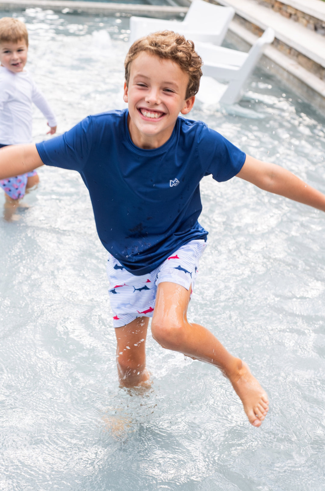 LITTLE BOY RUNNING IN WATER WEARING SHORT SLEEVE NAVY PERFORMANCE T-SHIRT WITH MARLIN PAINTING ON BACK 