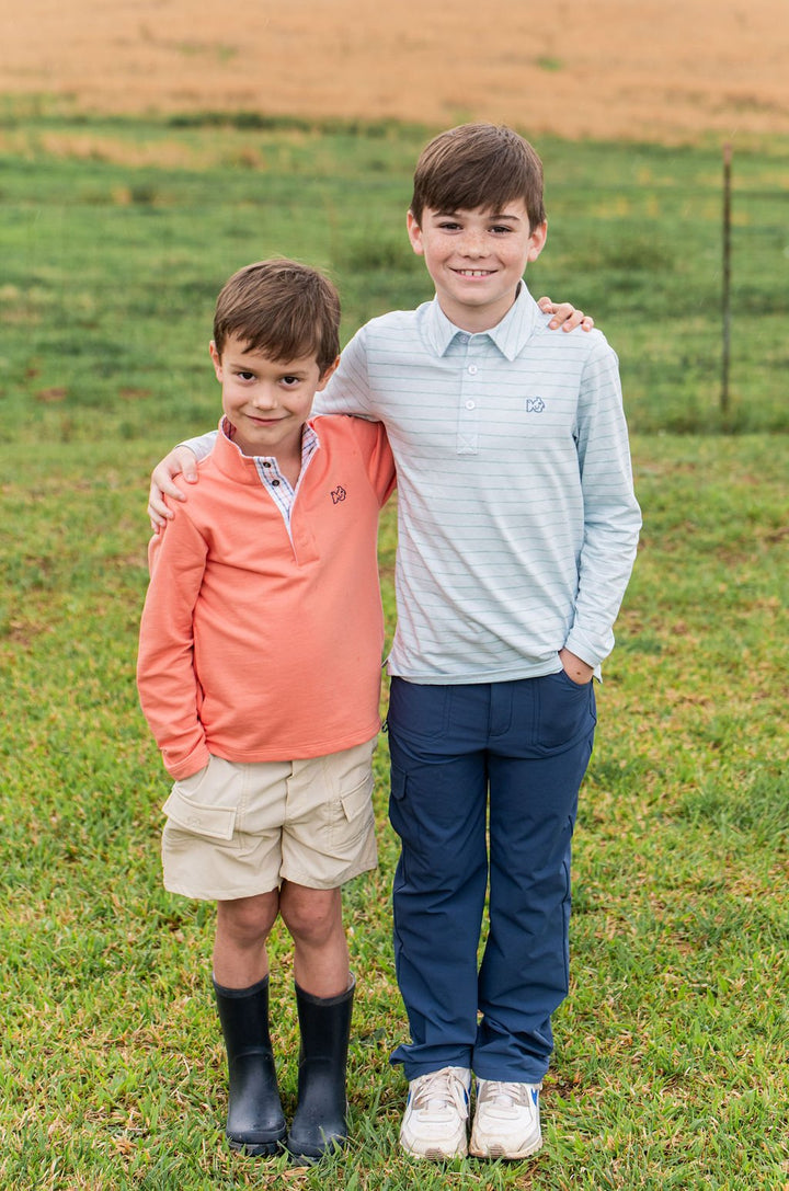 Two young boys standing in a grassy field, wearing casual clothing.