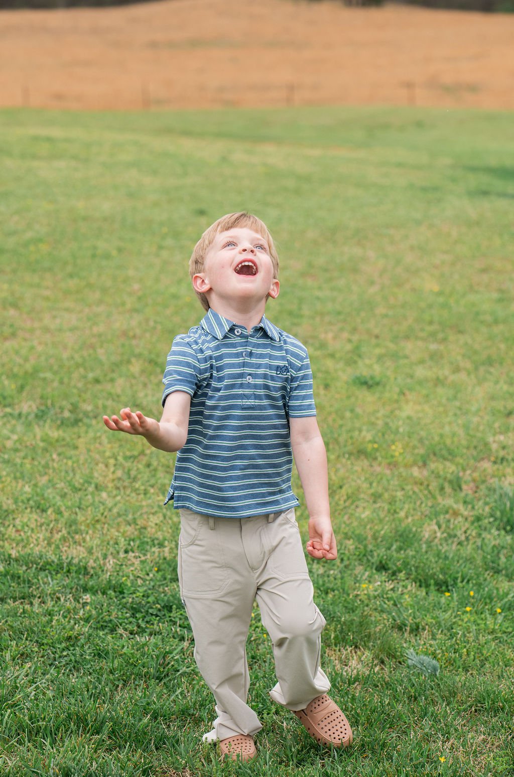 Child in a striped shirt and khaki pants standing in a grassy field
