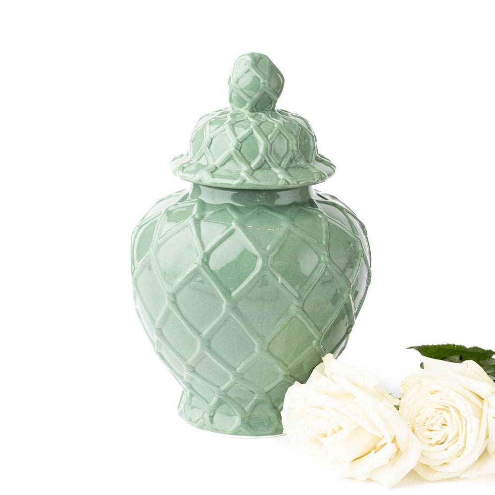 Green ceramic jar with a lid and white roses on a white background