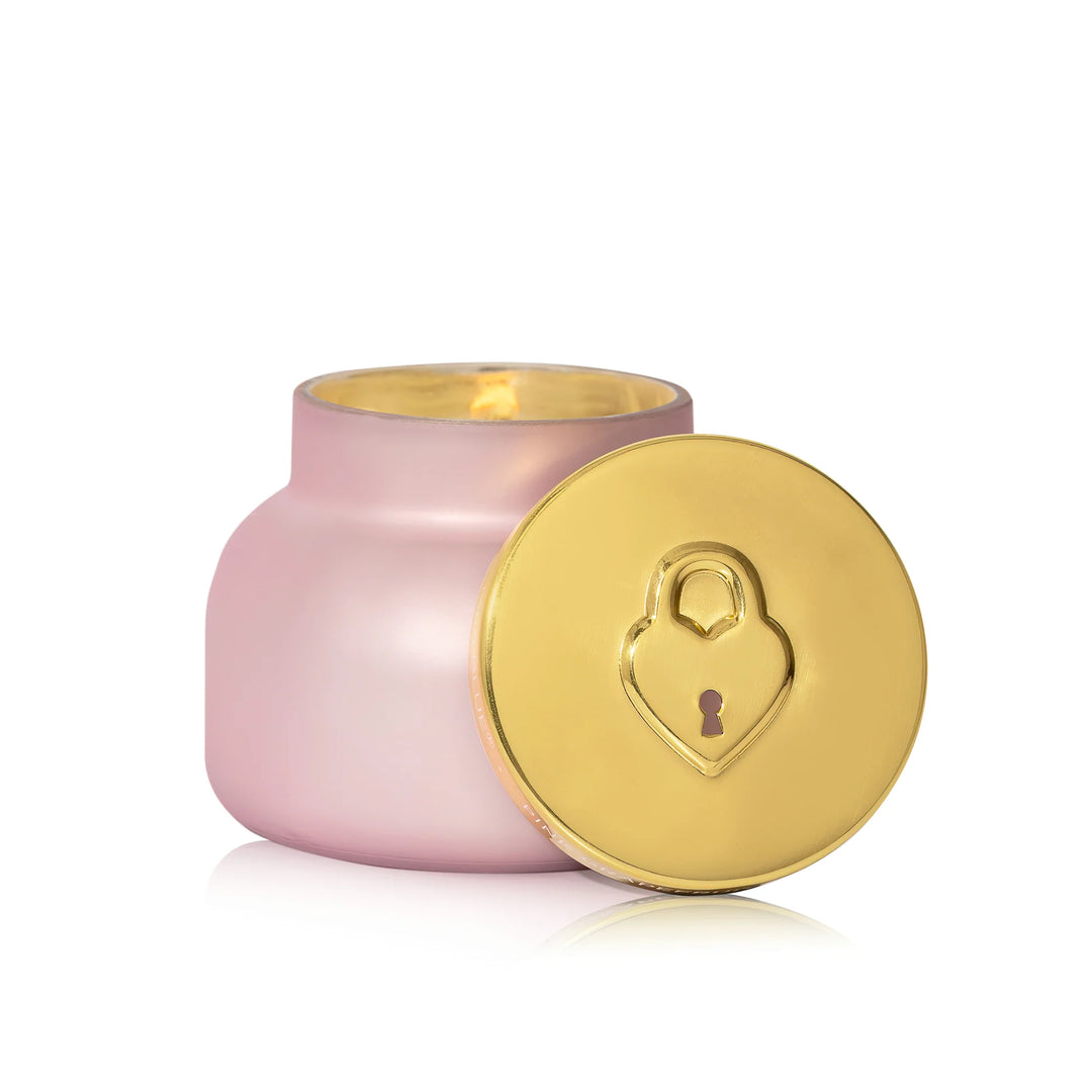 Pink candle with a gold lid featuring a heart-shaped lock design on a white background