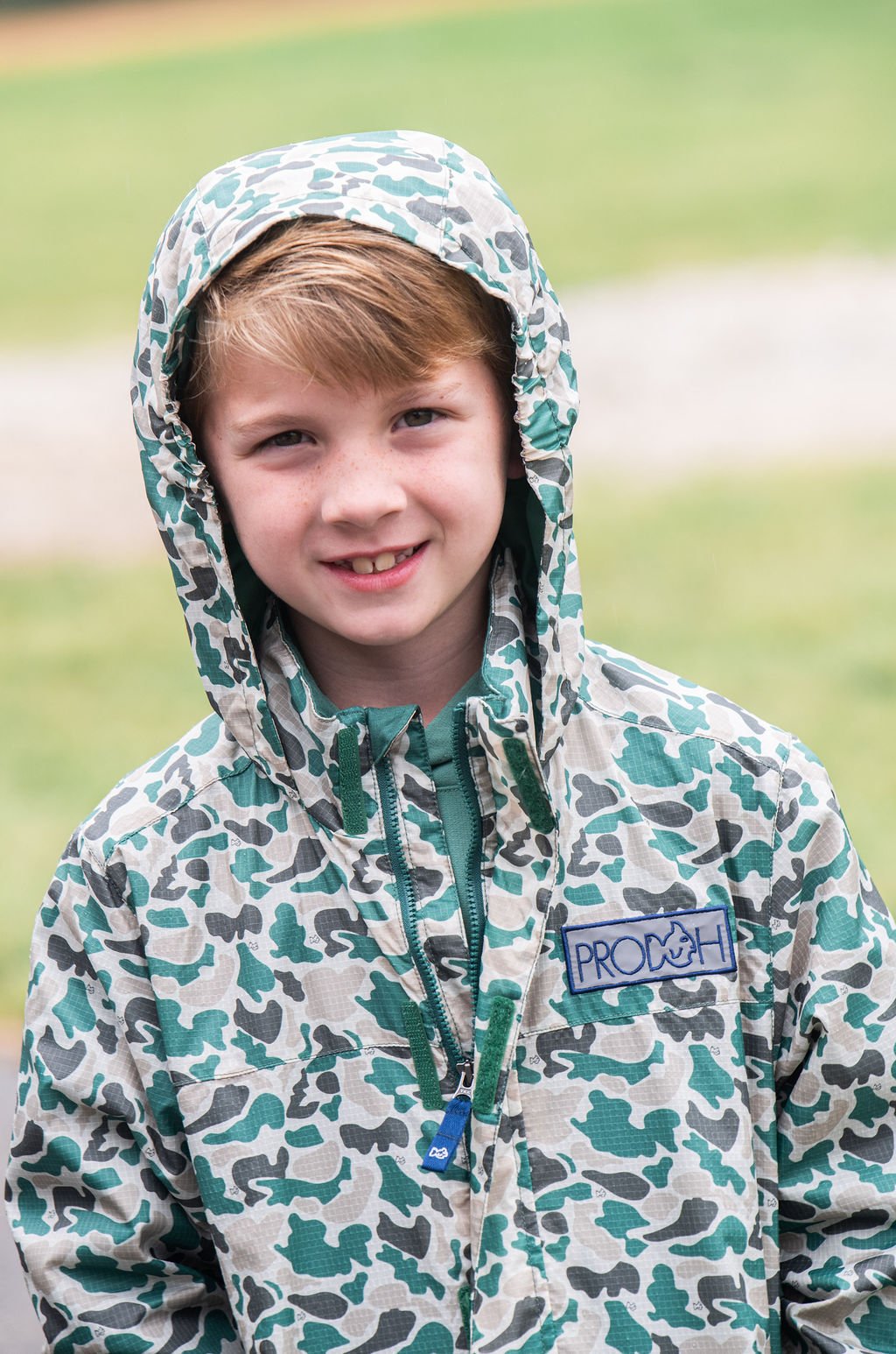 Child wearing a patterned raincoat with a visible brand logo outdoors.