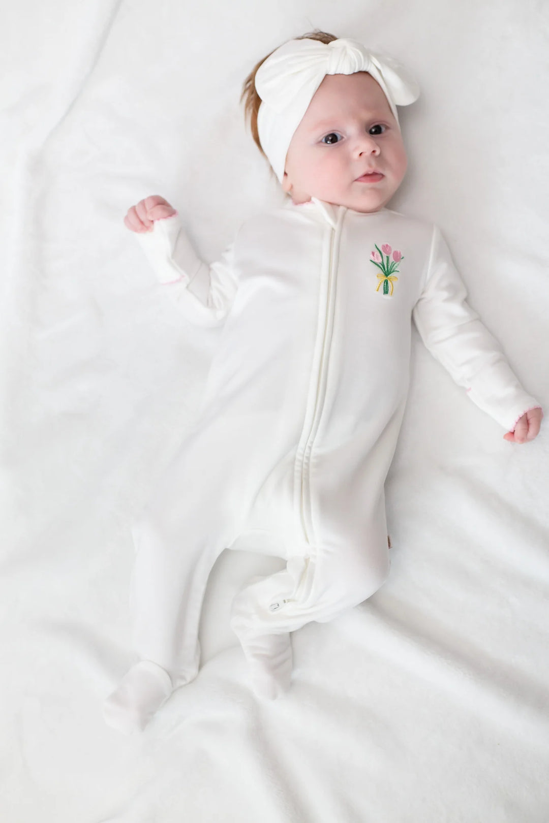 Baby in a white footie with a floral motif design on a white background