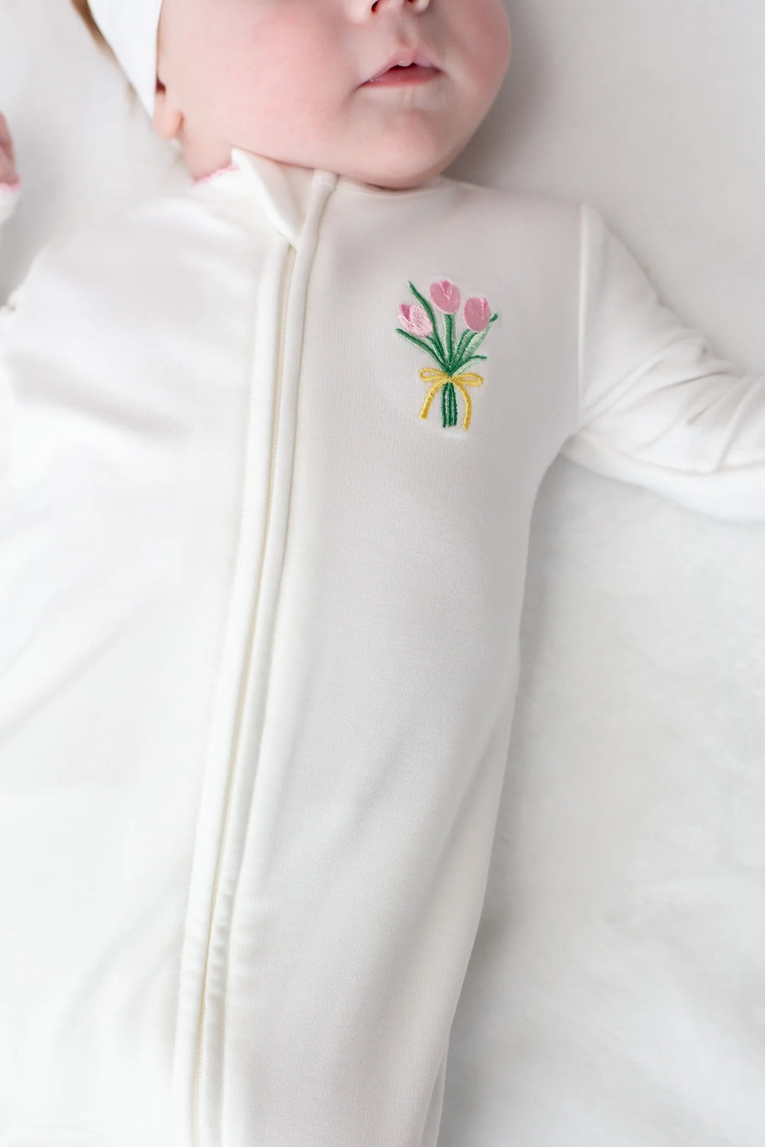 Baby in a white outfit with a floral motif design on a plain background