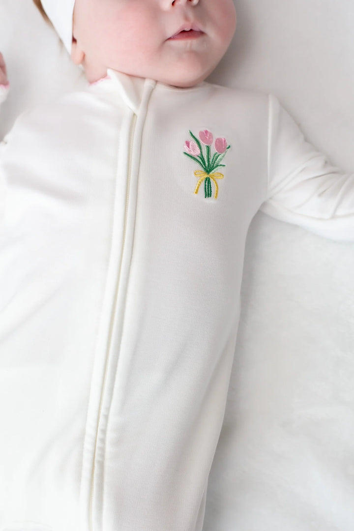 Baby in a white outfit with a floral motif design on a plain background