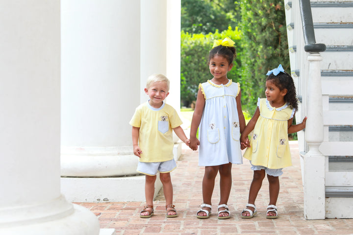 THREE CHILDREN EACH WEARING YELLOW AND BLUE PUPPY DESIGNED OUTFITS COORDINATING BY THE STAIRS ON BRICK