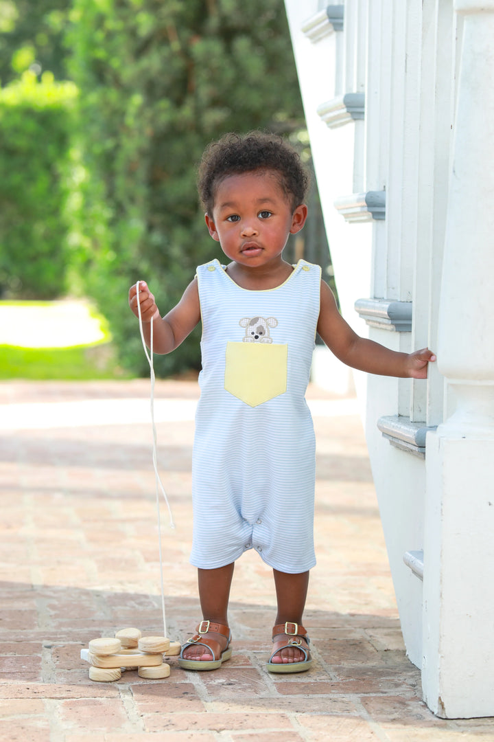 LITTLE BOY WEARING BLUE AND WHITE STRIPED JON JON WITH PUPPY IN POCKET DESIGN STANDING BY STAIRS PULLING A TOY
