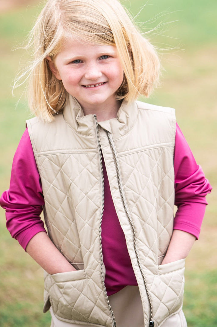 Young girl wearing a beige quilted vest over a pink shirt outdoors.