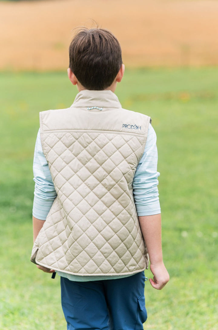 Child wearing a quilted vest outdoors on a grassy field