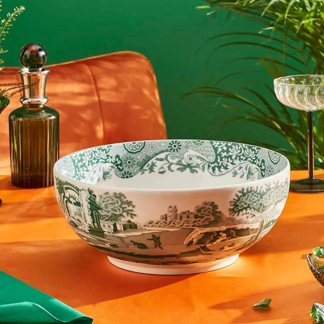 Decorative bowl with green and white pattern on an orange surface with a green wall and plant in the background.