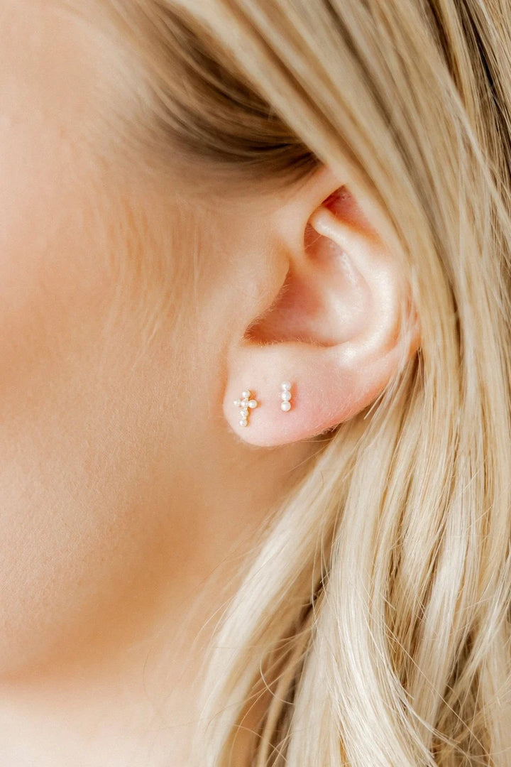 Clara pearl cross screwback stud earring worn on the ear as a dainty faith accessory