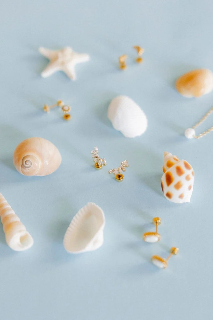 Delaney gold crystal screwback earrings styled with pearls and seashells on a blue background