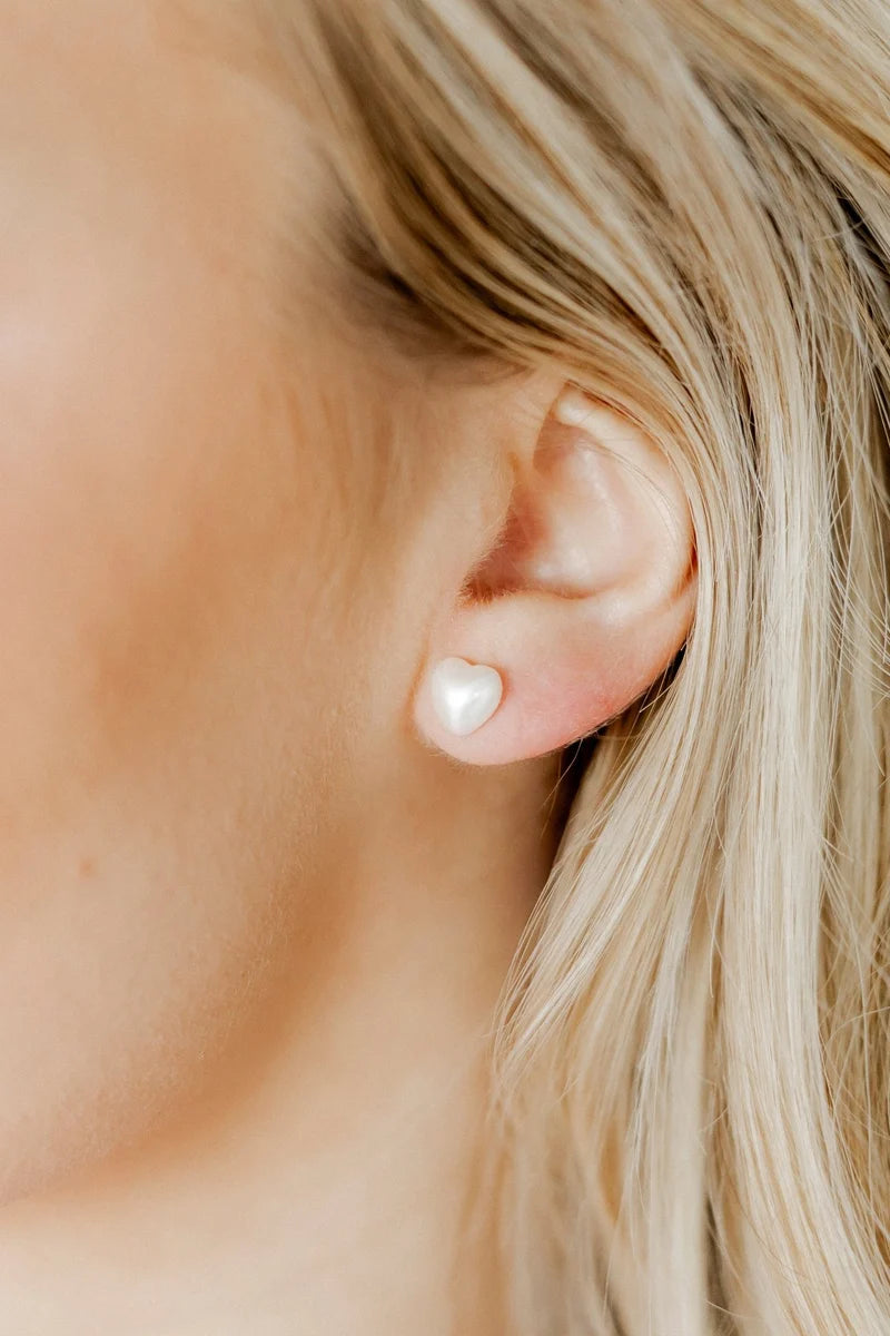 Pair of petite white pearl heart screwback stud earrings on a white background