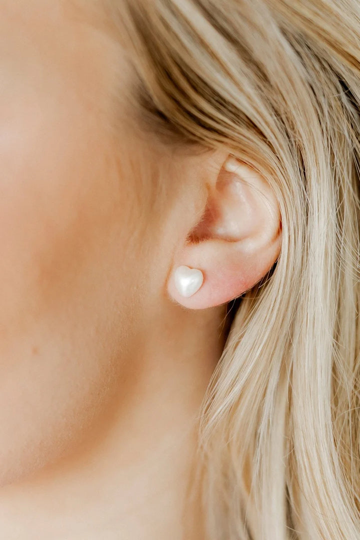 Pair of petite white pearl heart screwback stud earrings on a white background