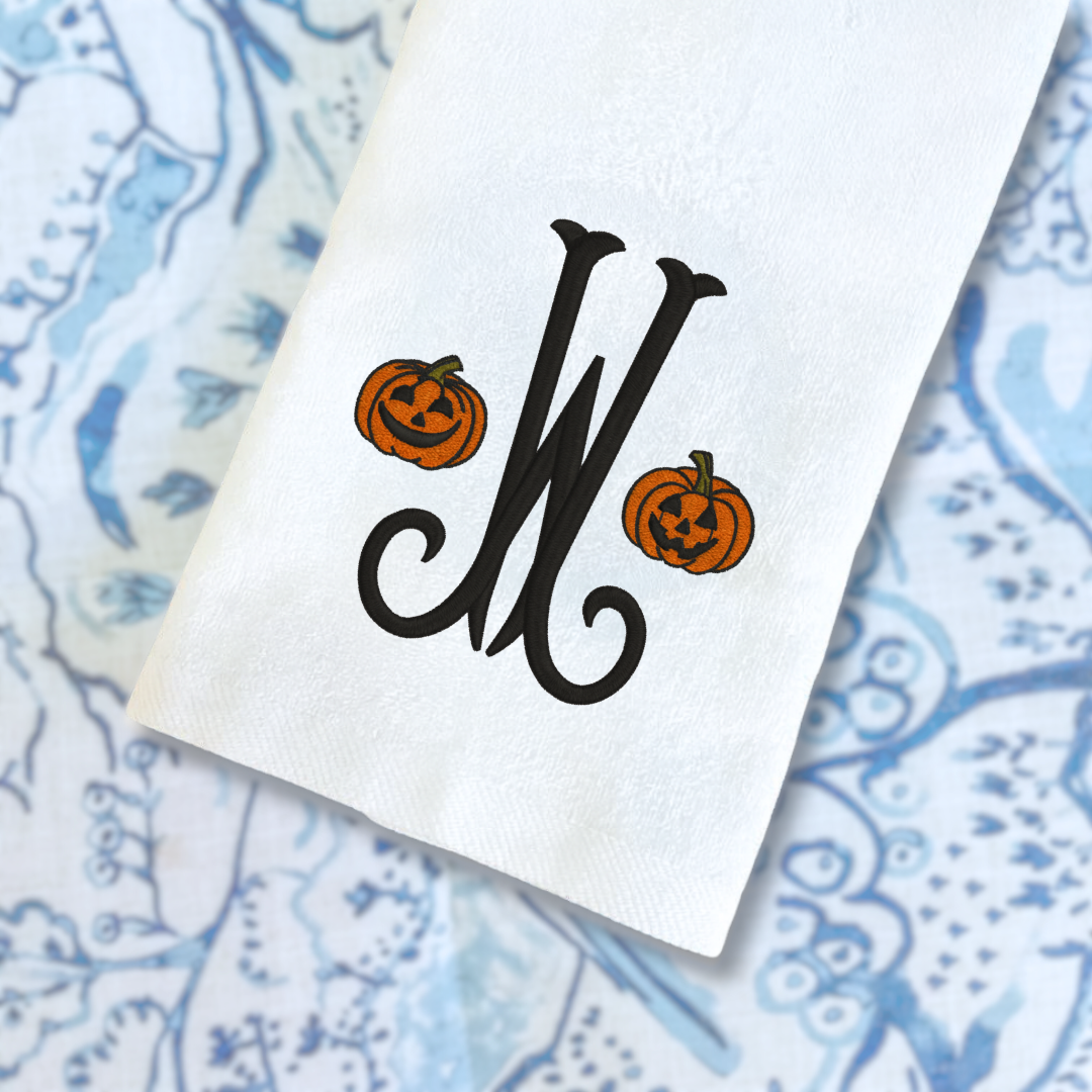 White napkin with black monogram 'W' and Halloween pumpkins on a blue patterned background