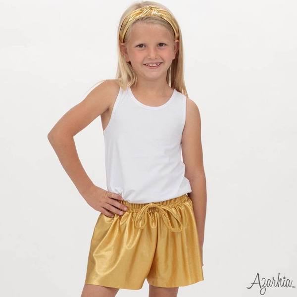 Young girl wearing a white tank top and gold shorts on a plain background