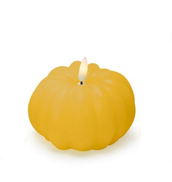 Yellow pumpkin-shaped candle between two decorative vases on a white background