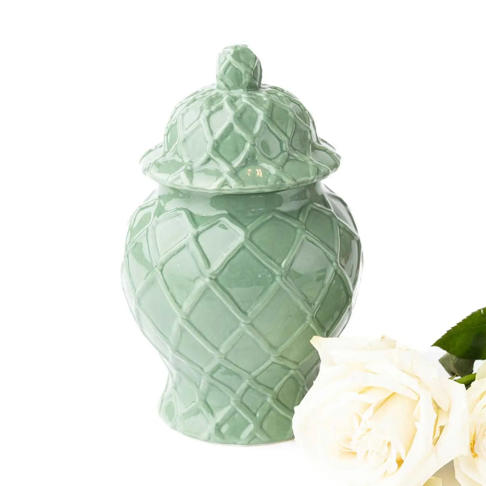 Green ceramic jar with a lid on a white background with a white rose.