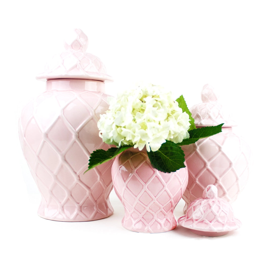 Set of pink ceramic jars with a lid and a smaller pink vase with flowers on a white background