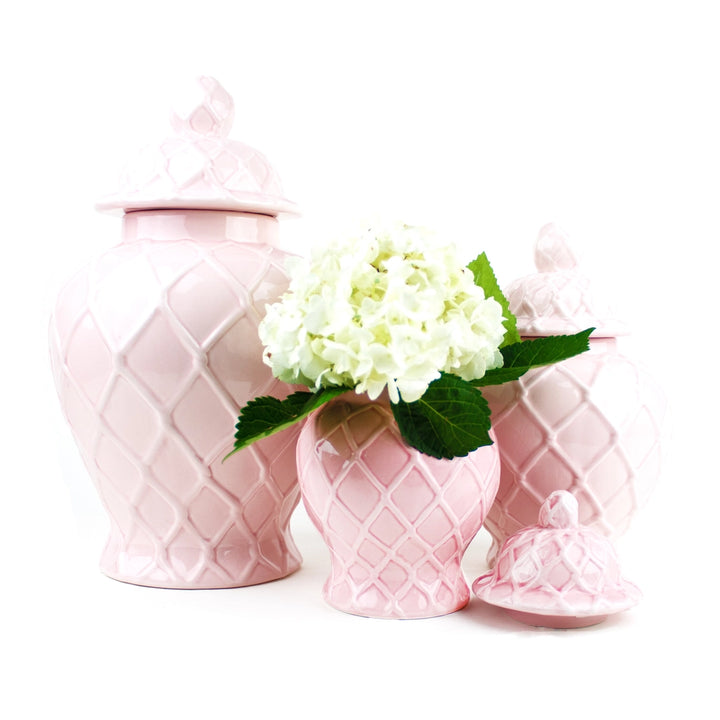 Set of pink ceramic jars with a lid and a smaller pink vase with flowers on a white background