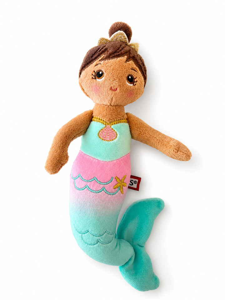 A plush mermaid doll toy with brown hair in a bun, a teal and pink gradient mermaid tail, and a small red tag on the side, shown on a plain white background.