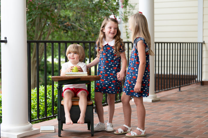 Three children in matching dresses standing on a porch.