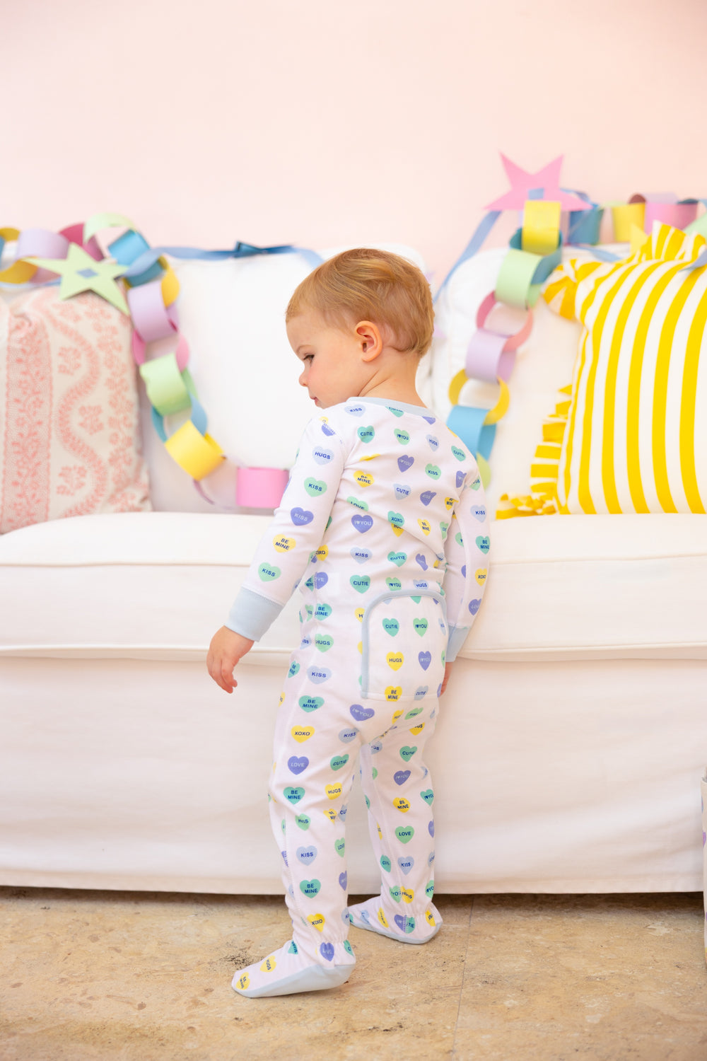 WHITE LONG SLEEVE FOOTIES WITH BLUE/GREEN HEARTS AND BLUE TRIM ON LITTLE BOY BY COUCH