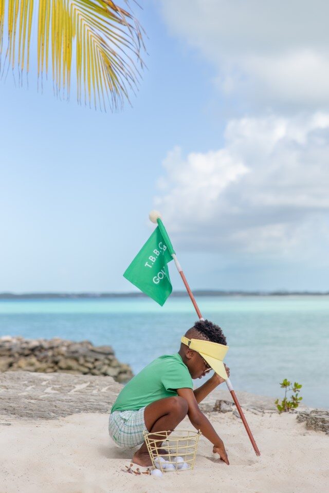 LITTLE BOY ON BEACH WITH GOLF BALLS AND GREEN FLAG WEARING GREEN CREWNECK T-SHIRT