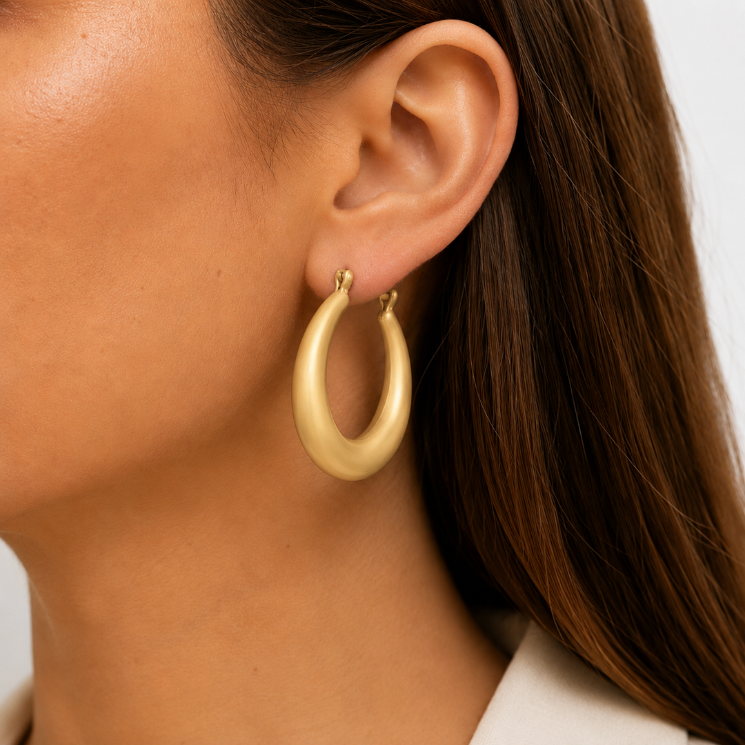 Gold hoop earrings worn by a person with a neutral background