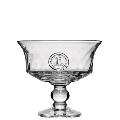 A clear mouth-blown glass compote dish with a hand-stamped monogrammed medallion on the side.